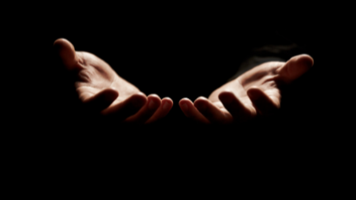 Hænder strakt ud i en velkomnende eller bedende gestus mod en mørk baggrund.