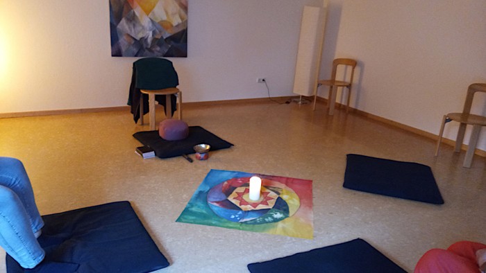 Ein Raum mit einer Kerze in der Mitte und Stühlen drum herum.