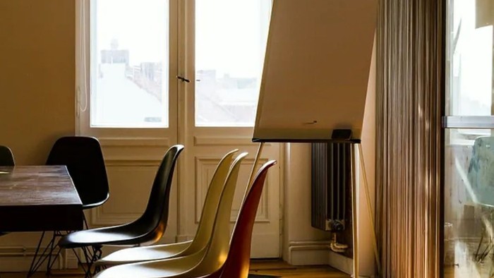 Helles Zimmer mit Vintage-Stühlen, Holzboden, großer Weißwandtafel und natürlichem Licht, das durch die Fenster strömt.