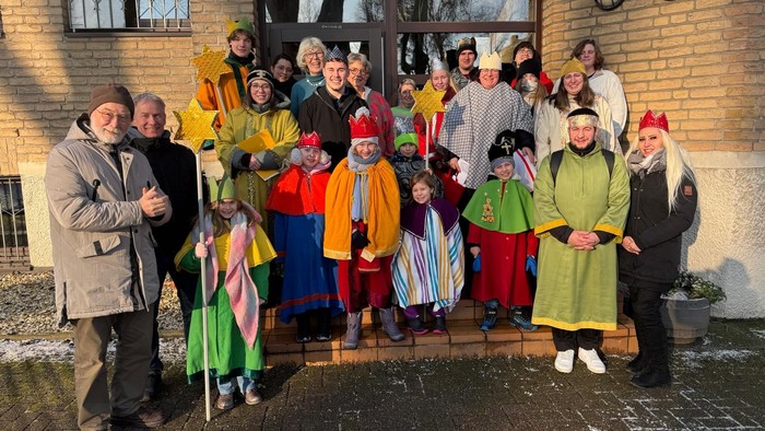 Gruppe von Menschen in farbenfrohen Kostümen und Winterkleidung, die draußen vor einem Backsteingebäude posieren.