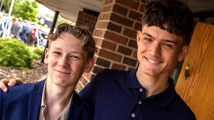 To smilende unge mænd i blå skjorter med en tekst, der opfordrer til genbrug af konfirmationstøj til fester.