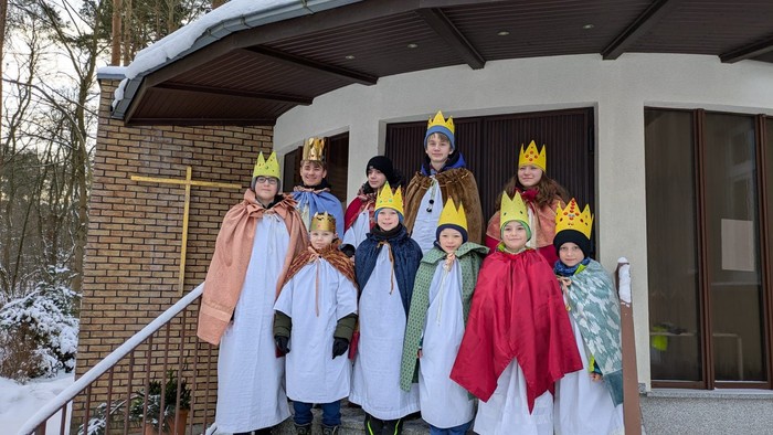 Kinder, verkleidet als Könige in farbenfrohen Roben und Kronen, posieren gemeinsam vor einem Gebäude im Winter.