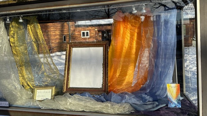 Verpackte Kunstwerke und ein gerahmter Spiegel, ausgestellt in einem Schutzgehäuse draußen, mit Plastik abgedeckt.