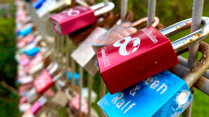 Bunte Liebesschlösser, die an einem Metallzaun in einer Außenumgebung befestigt sind.