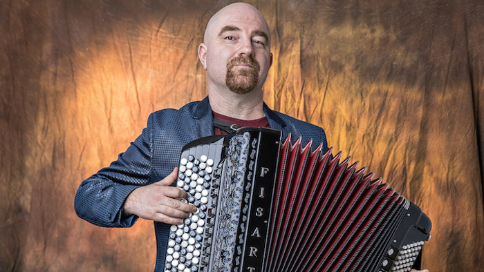 Ein Mann im Anzug spielt mit ernstem Gesichtsausdruck ein großes Akkordeon mit der Aufschrift „FisArt“.