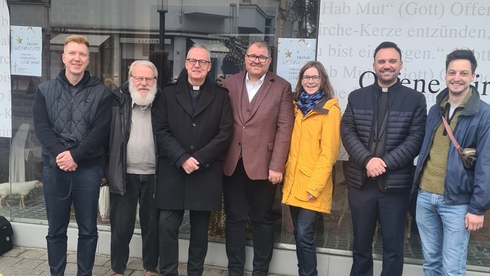 Eine Gruppe von sieben Personen, die vor einem Gebäudeeingang bei einer formellen Veranstaltung oder einem Event posieren.