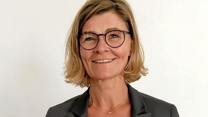 En kvinde med kort hår og briller, smiler til kameraet.