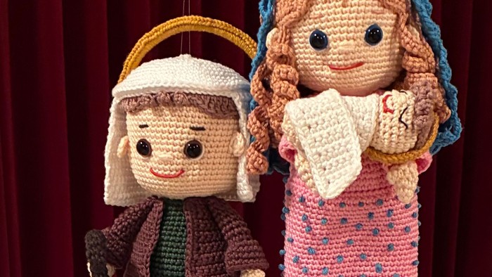 Hæklede dukker klædt ud som bibelske figurer med ruller, ophængt mod en rød baggrund.