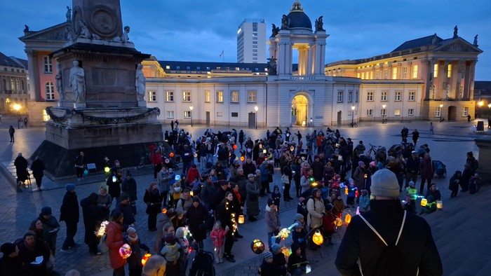 Menschen versammeln sich auf einem Platz und halten Laternen während einer Abendveranstaltung in der Nähe historischer Architektur.