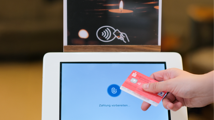 Kontaktlose Kartenzahlung an einer digitalen Spendenbox mit EC‑Karte vor Kerzenlicht.