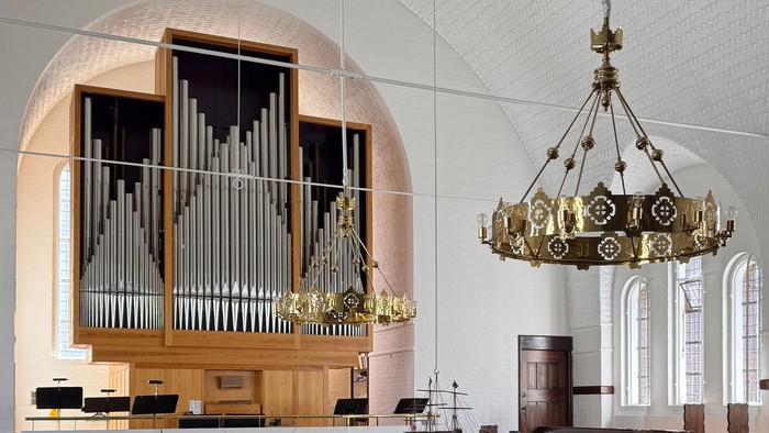 Elegant kirkeinteriør med træbænke, et pibeorgel og prægtige lysekroner.