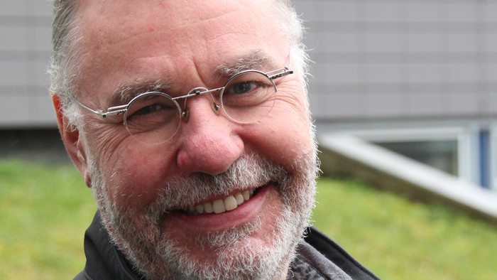 Hans-Peter Naumann ist Pfarrer und unterrichtet Religion an einer Schule. Er trägt eine runde Brille und kurzes, graues Haar und einen kurzen Vollbart. Hans-Peter Naumann lächelt auf dem Bild.