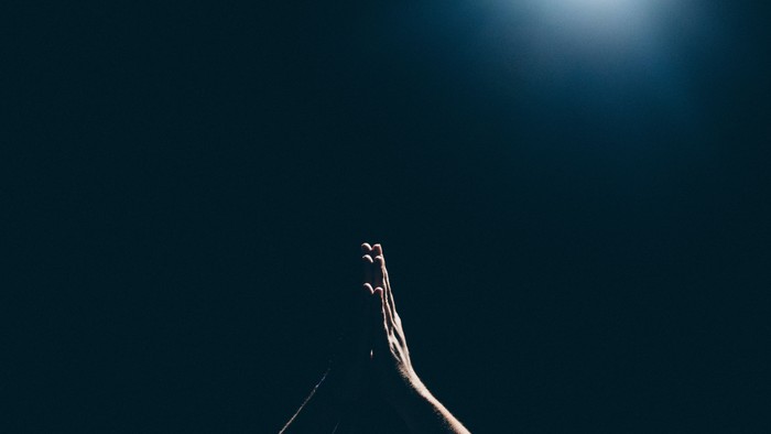 A person's hand reaching towards a bright light in a dark background.