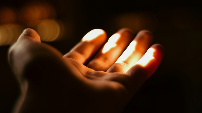 Eine Hand hält ein leuchtendes Objekt im Dunkeln.