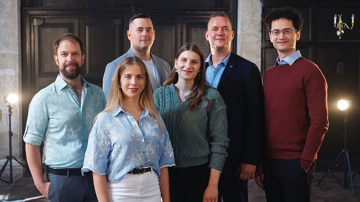 Eine Gruppe von sechs Personen, die in einem stilvollen, gut beleuchteten Innenraum posieren.