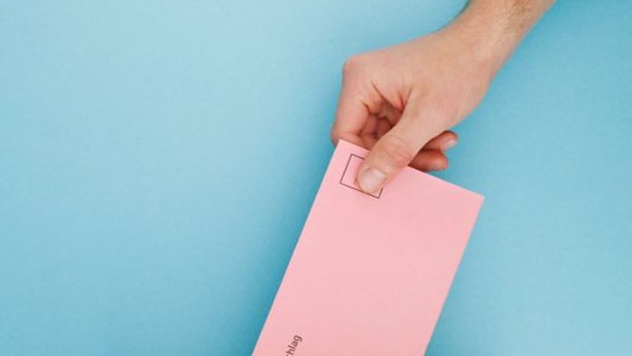 Hand steckt rosafarbenen Brief in Kartonbox