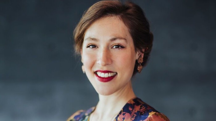 En glad kvinde i en farverig blomstret bluse, der smiler varmt til kameraet.