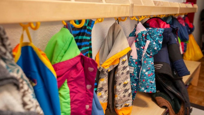 Bunte Kinderjacken und Mäntel ordentlich an Wandhaken aufgehängt.