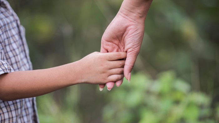 Kind wird von einer Frau an die Hand genommen