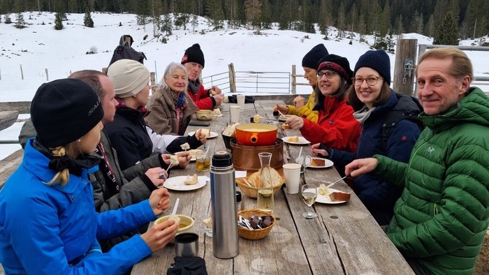 Die Gruppe, die sich für die Schneeschuhwanderung in La Givrine getroffen hat sitzt an einem Holztisch und isst