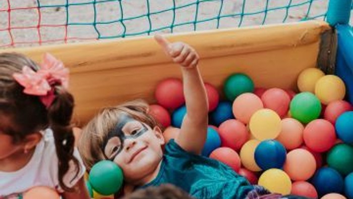 Børn leger gladt i en farverig oppustelig boldgrav, hvor et barn har en sjov ansigtsmaske på.