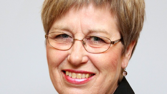 Professionel kvinde med briller, sort jakke og en dekorativ nål, der smiler varmt.