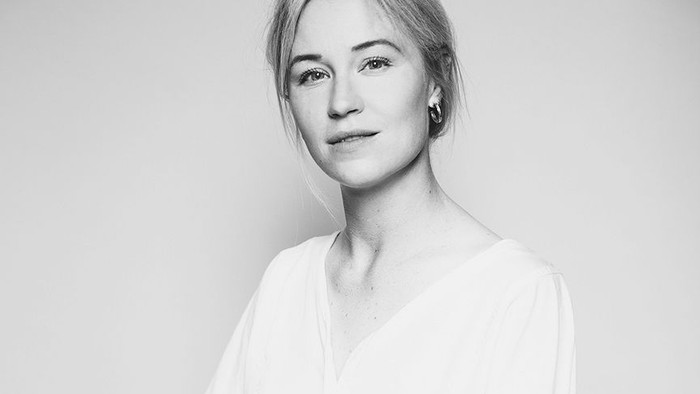 En afbalanceret kvinde i en hvid bluse og sorte bukser sidder selvsikkert på en skammel.