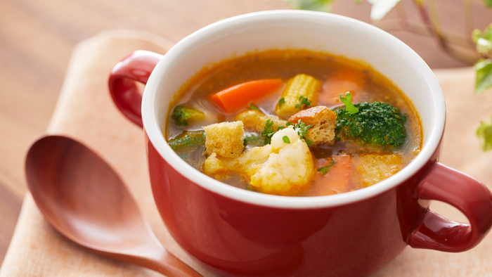 Warm bowl of creamy vegetable soup with carrots, broccoli, and potatoes, served in a red ceramic mug.