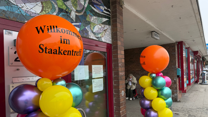Zwei Balonsäulen, oben ein großer orangefarbener Ballon mit der Aufschrift 