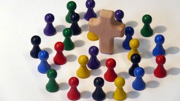 Farbenfrohe Holzfiguren um ein hölzernes Kreuz angeordnet