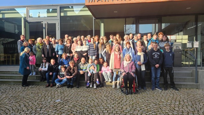 Eine vielfältige Gruppe von Menschen, darunter Kinder und Erwachsene, die gemeinsam vor dem Eingang eines modernen Gebäudes posieren.