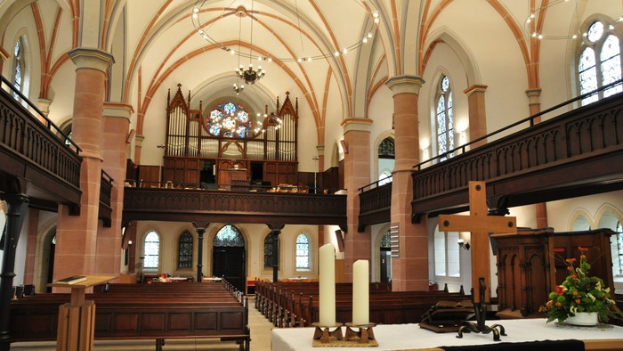 Elegante historische Kircheninnenausstattung mit hölzernen Kirchenbänken, einer prunkvollen Orgel und hohen Gewölbedecken mit Buntglasfenstern.
