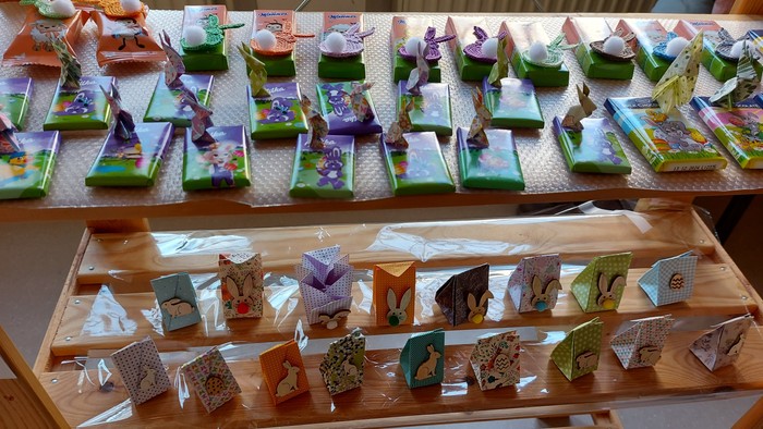 Bunte handgefertigte Geschenkboxen in Vogelhausform und Dekorationsartikel, ausgestellt auf Holzregalen.