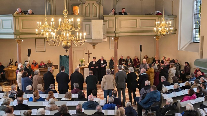 In einer hell erleuchteten Kirche sitzen viele Menschen und eine große Grppe steht am Altar.