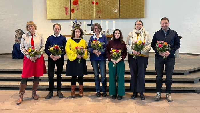 Gruppe von sieben Personen, die Blumensträuße in einer Kirche oder Kapelle halten.