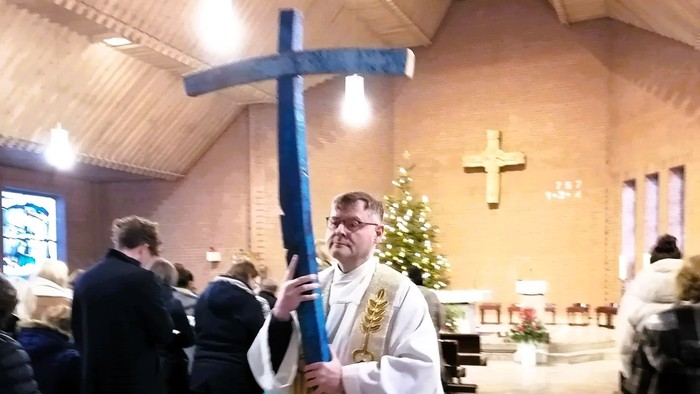 Pfarrer Hahner tragt ein großes Kreuz aus Holz in Dunkel- und Hellblau.