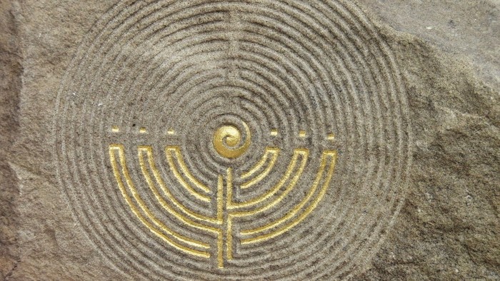 Das Bild zeigt eine goldene Menora auf einem steinernen Hintergrund.