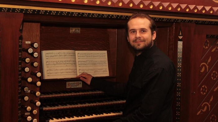 En mand spiller på et prægtigt orgel med noder foran sig.