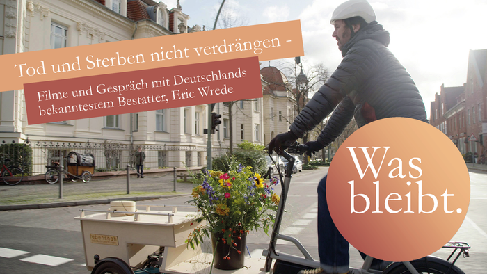 Man sieht einen Mann auf einem Lastenfahrrad, der Korb vorne trägt eine Urne und Blumenschmuck.