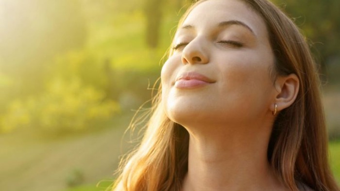 Frau, die mit geschlossenen Augen in der Natur steht und tief einatmet