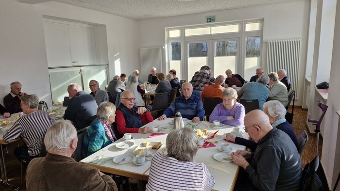 Eine Gruppe älterer Menschen versammelte sich um Tische und genoss eine Mahlzeit sowie Gespräche in einem Gemeinschaftsesszimmer.