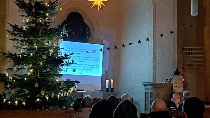 Im Innenraum der Johanneskirche, man sieht eine Leinwand mit Liedtext und einige Besucher in den Kirchenbänken.