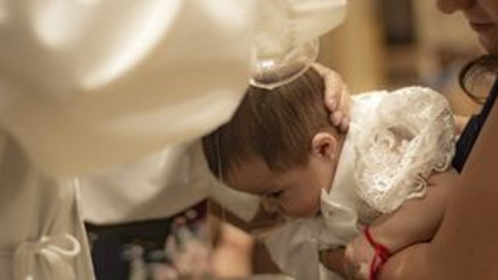 Ein kleines Kind in einem weißen Kleid und einer Tiara erhält während einer religiösen Zeremonie einen Segen.