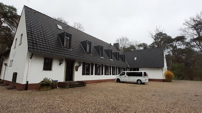 Ein großes, weißes Haus mit schwarzem Dach und einem geparkten weißen Van davor.