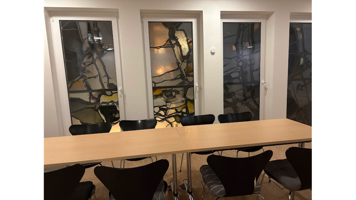 Langer Tisch mit Stühlen steht vor den Fenstern.