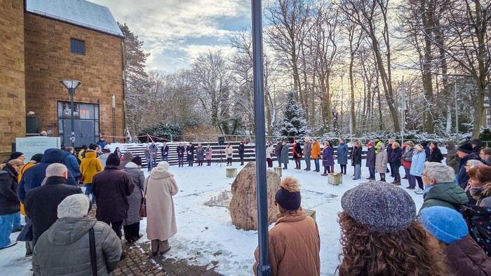 Eine Menschenmenge steht im Kreis um eine Gedenkstätte. Es liegt Schnee.