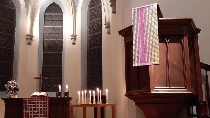 Elegante Kircheninnenausstattung mit einem Altar mit Kerzen, bunten Glasfenstern und einem hölzernen Lesepult mit einem farbenfrohen Banner.