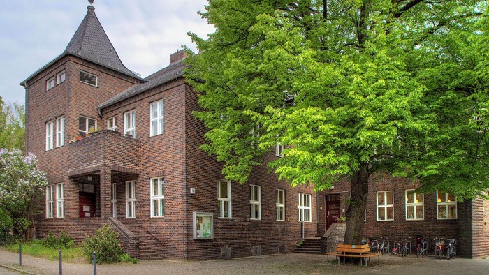 Ein historisches Backsteingebäude mit Turm, umgeben von üppigem Grün und einer Außenbereich-Sitzfläche.