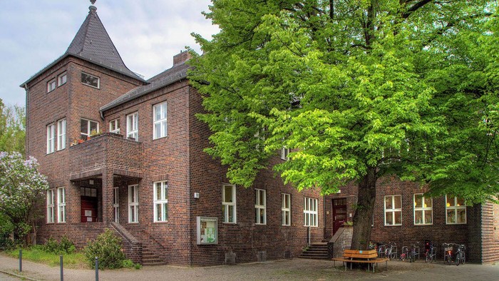 Ein historisches Backsteingebäude mit Turm, umgeben von üppigem Grün und einer Außenbereich-Sitzfläche.