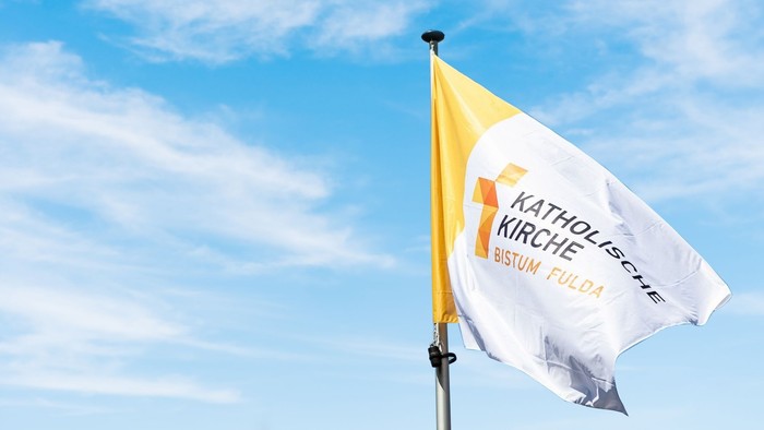 Eine gelb-weiße Flagge, die das katholische Bistum Fulda repräsentiert, vor einem blauen Himmel.